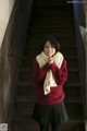 A woman in a red sweater and black skirt standing on a set of stairs.